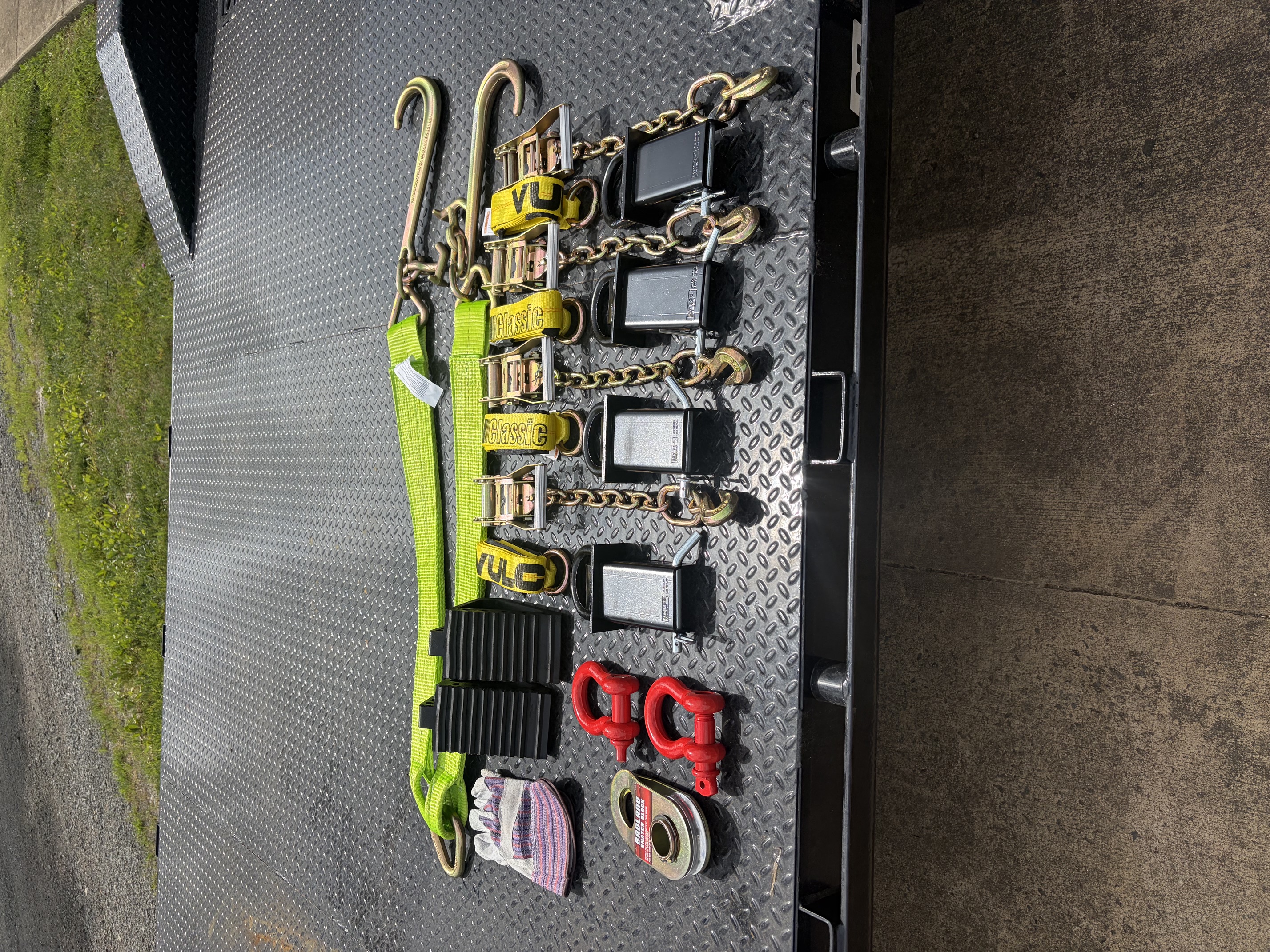 Included tie-down equipment: ratchet straps, chains, D-rings, red shackles, and gloves laid out on diamond plate